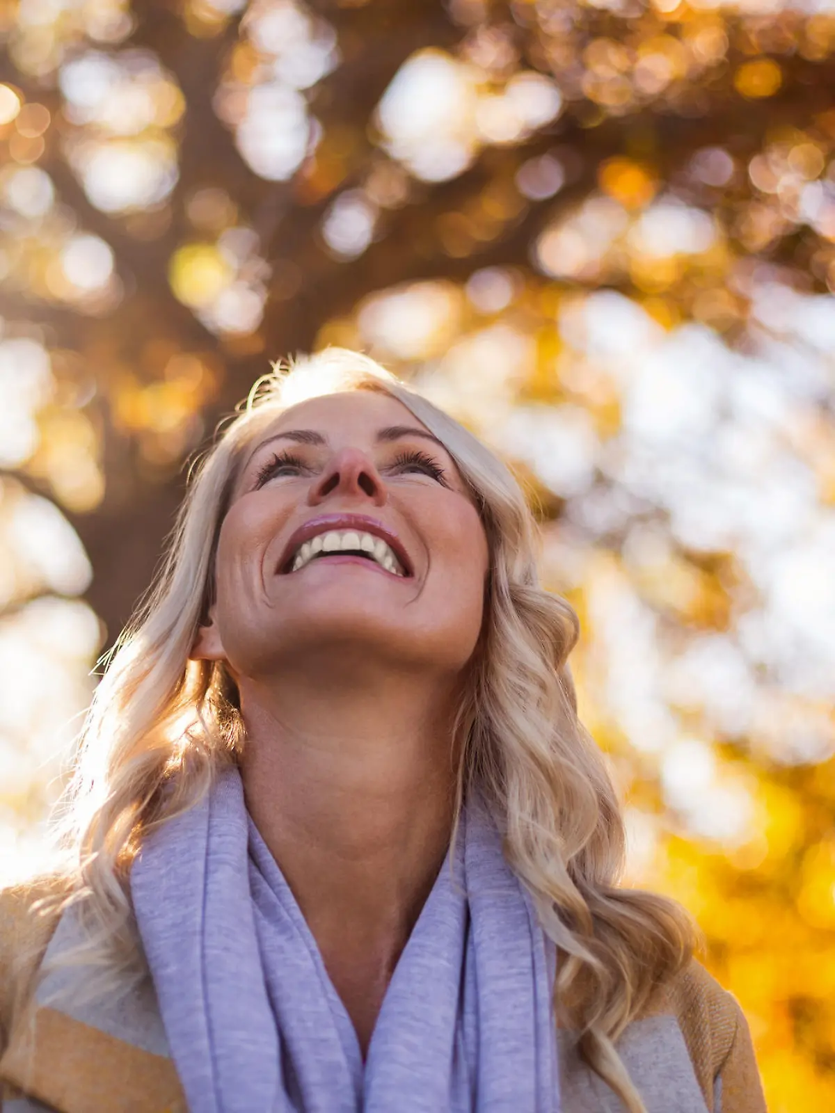 Smiling woman looking up against trees at park during autumn