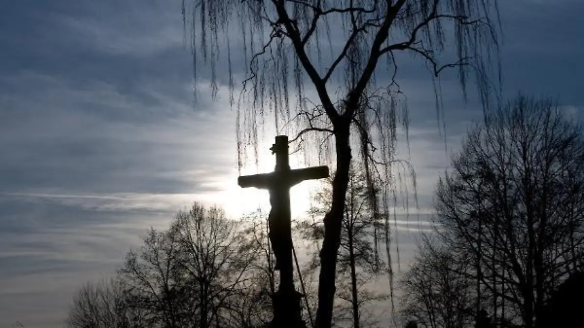 Ein Grabkreuz steht am Sonntag (25.01.2009) auf einem Friedhof in Fürstenau (Landkreis Osnabrück) im Gegenlicht der untergehenden Sonne vor einer Trauerweide. Foto: Friso Gentsch dpa/lni  +++(c) dpa - Report+++
