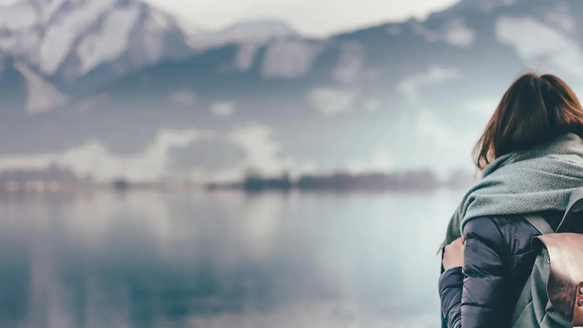 Hipster young girl with backpack enjoying landscape standing near the lake.