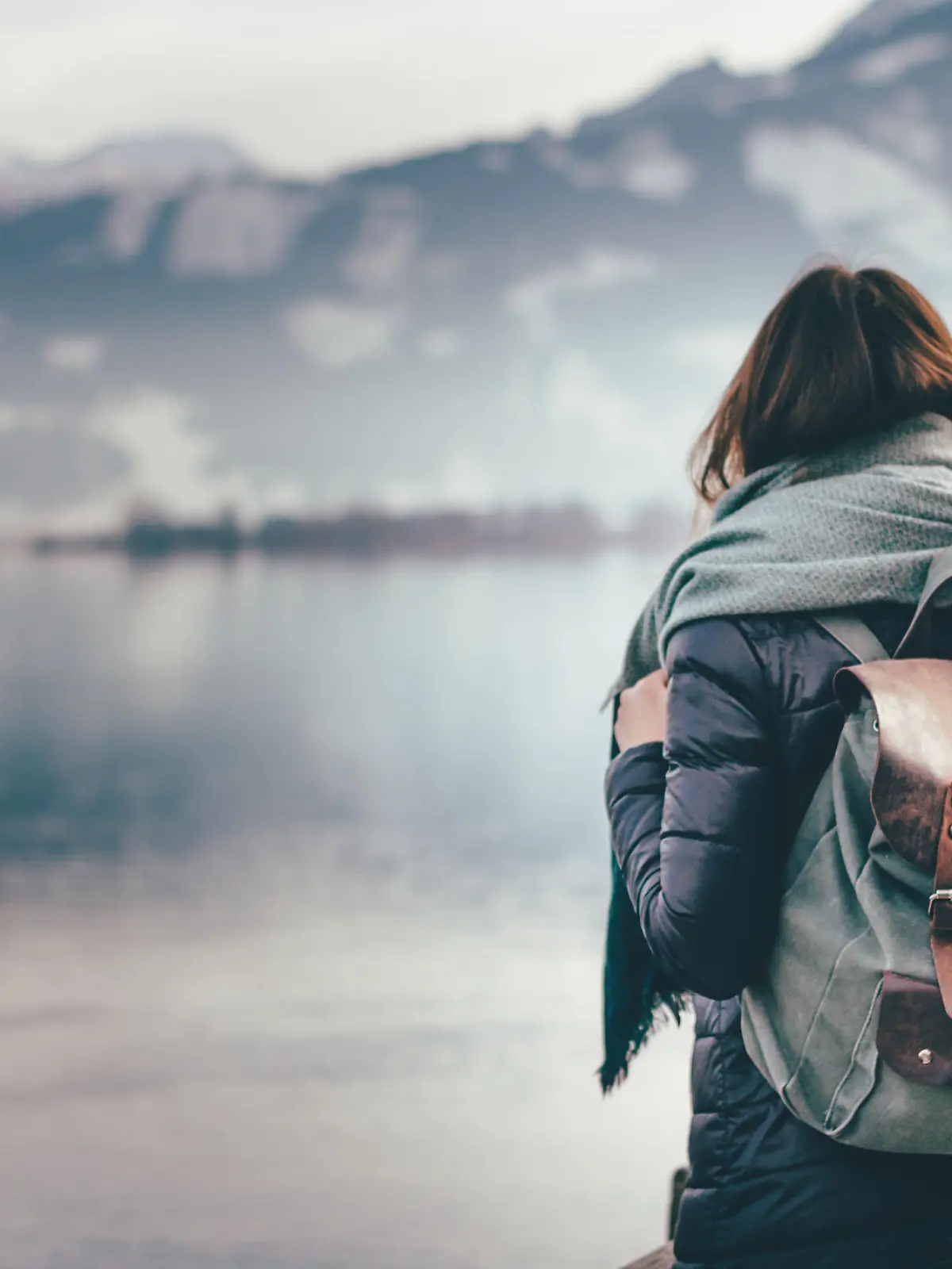 Hipster young girl with backpack enjoying landscape standing near the lake.