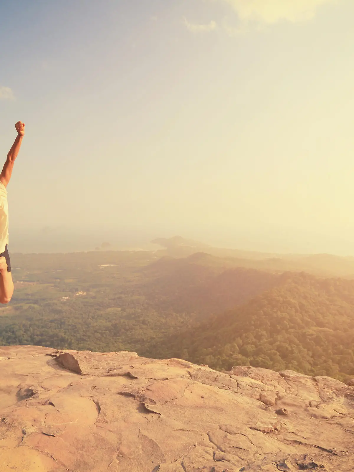 cheering young asian woman jumping on mountain peak rock