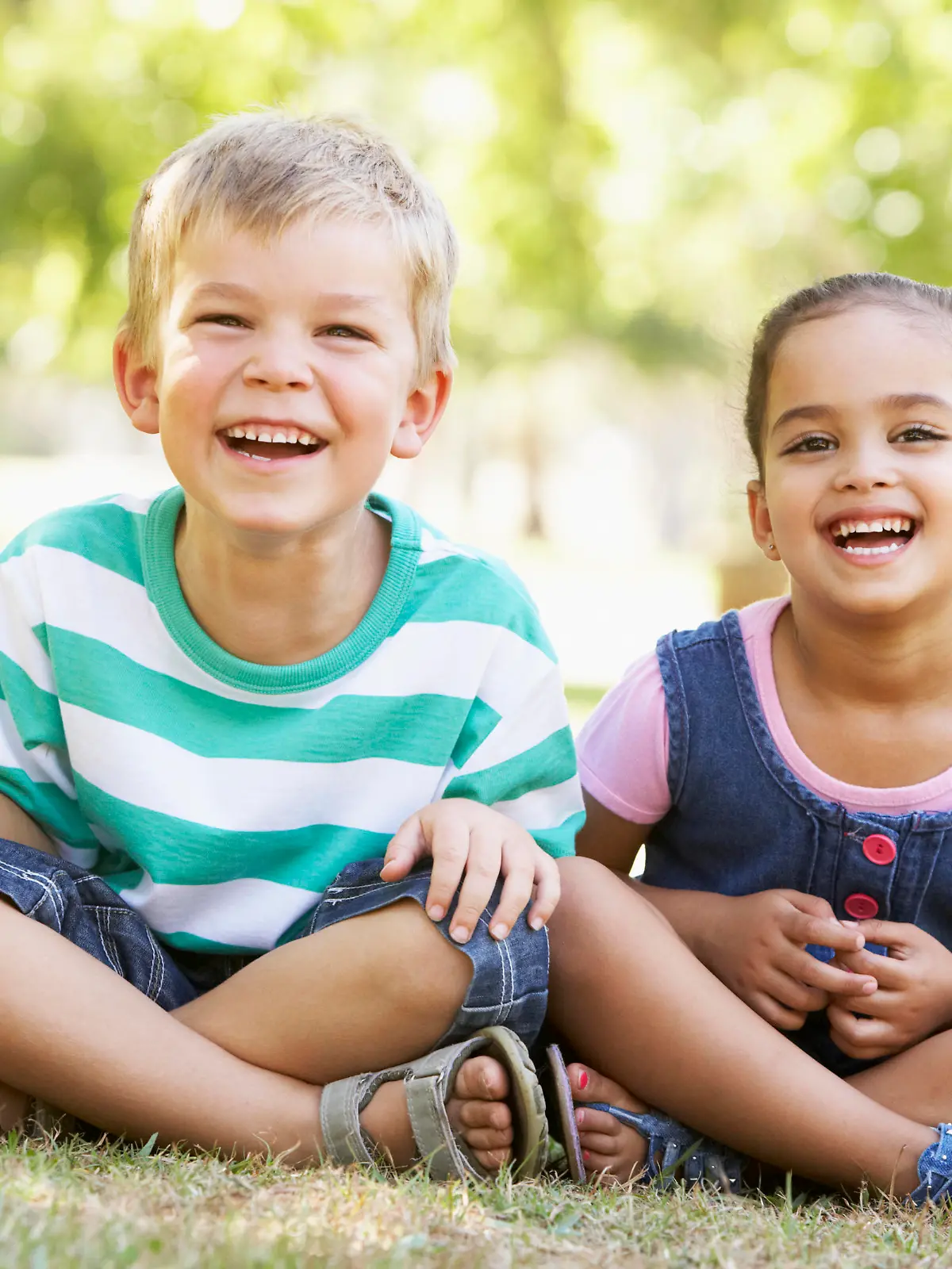 Two Children Playing Together In Park Sitting On Grass Smiling