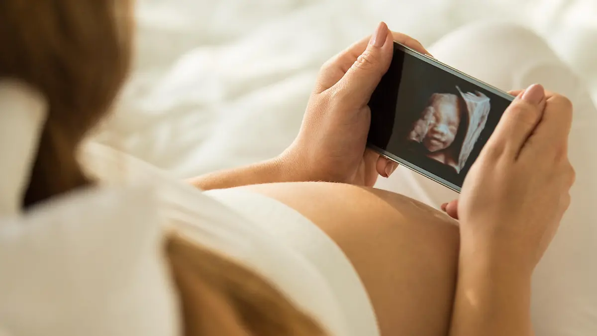 Pregnant mid adult woman holding a smart phone that shows the 3D ultrasound picture of her baby.
