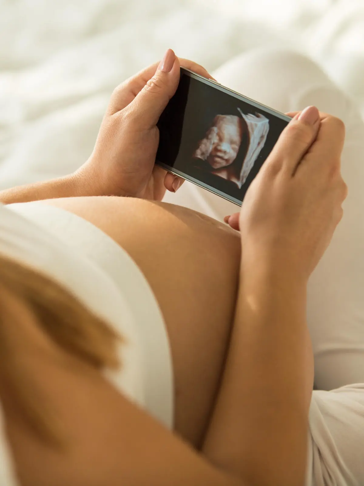 Pregnant mid adult woman holding a smart phone that shows the 3D ultrasound picture of her baby.