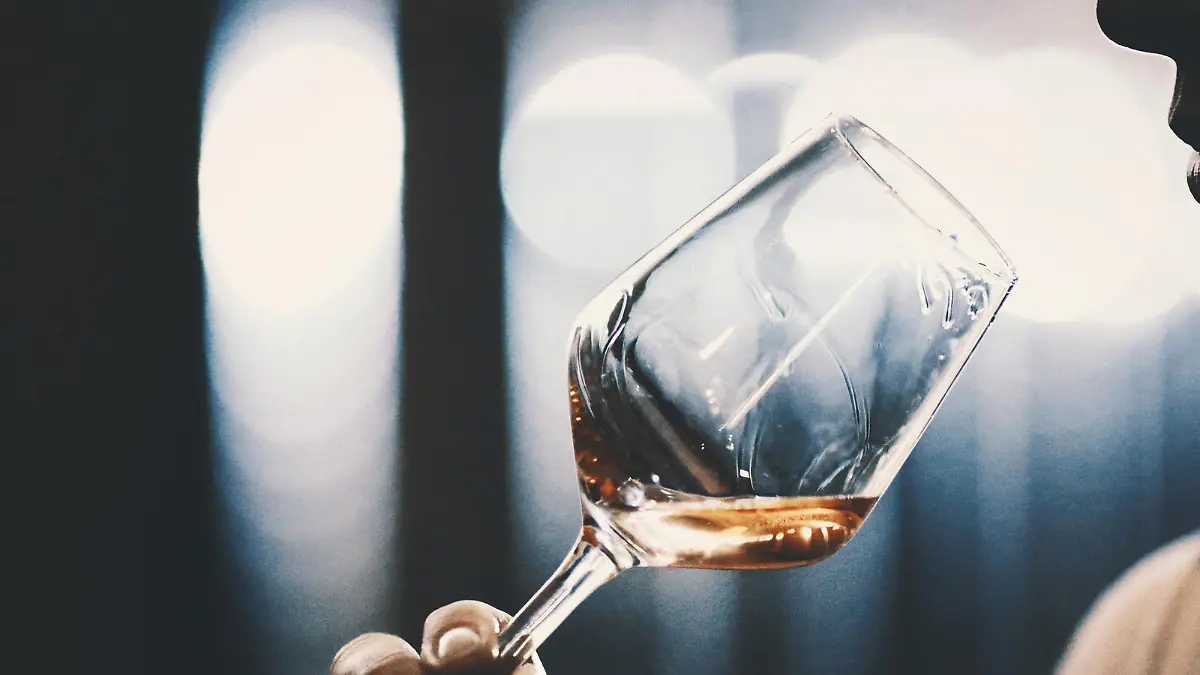 Closeup of unrecognizable adult man slightly swirling a glass of rose wine under his nose and trying to catch bouquet. She's in a wine cellar, there are blurry metal tanks in background. Backlit