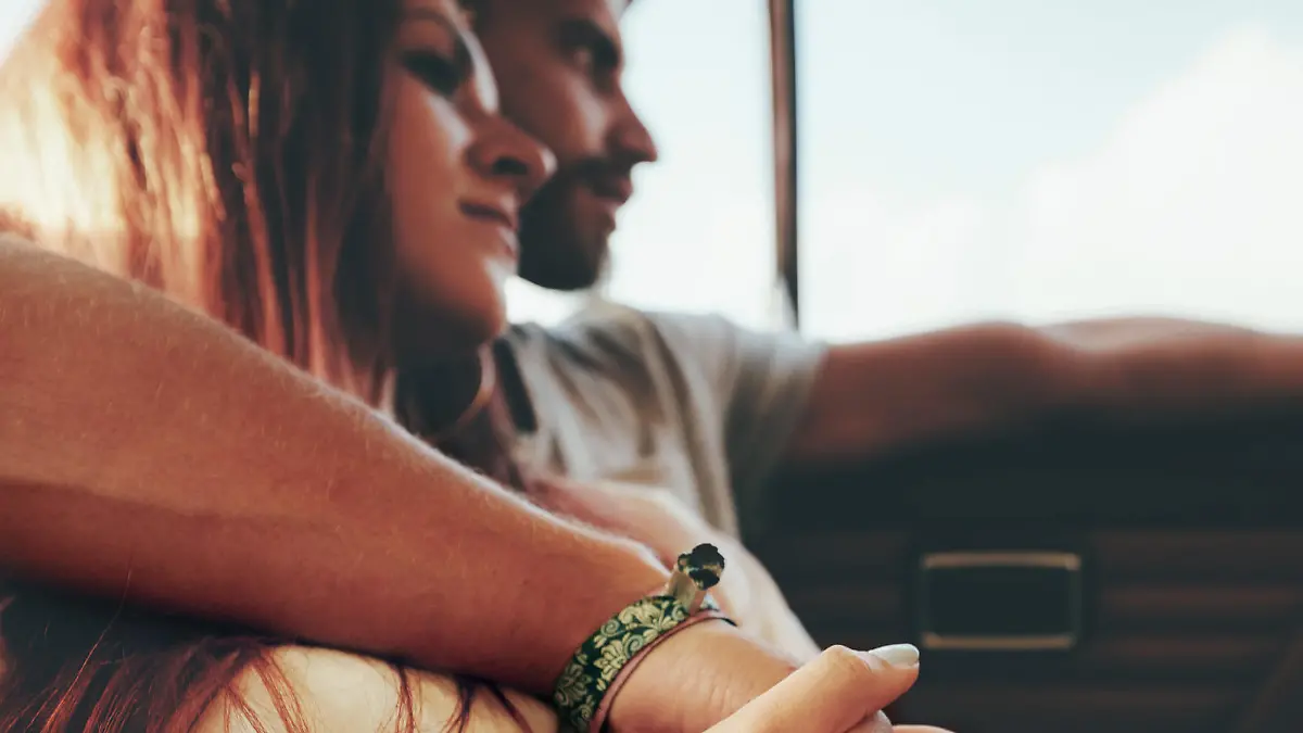 Affectionate young couple sitting in back seat of a car going on road trip. Focus on couple holding hands.