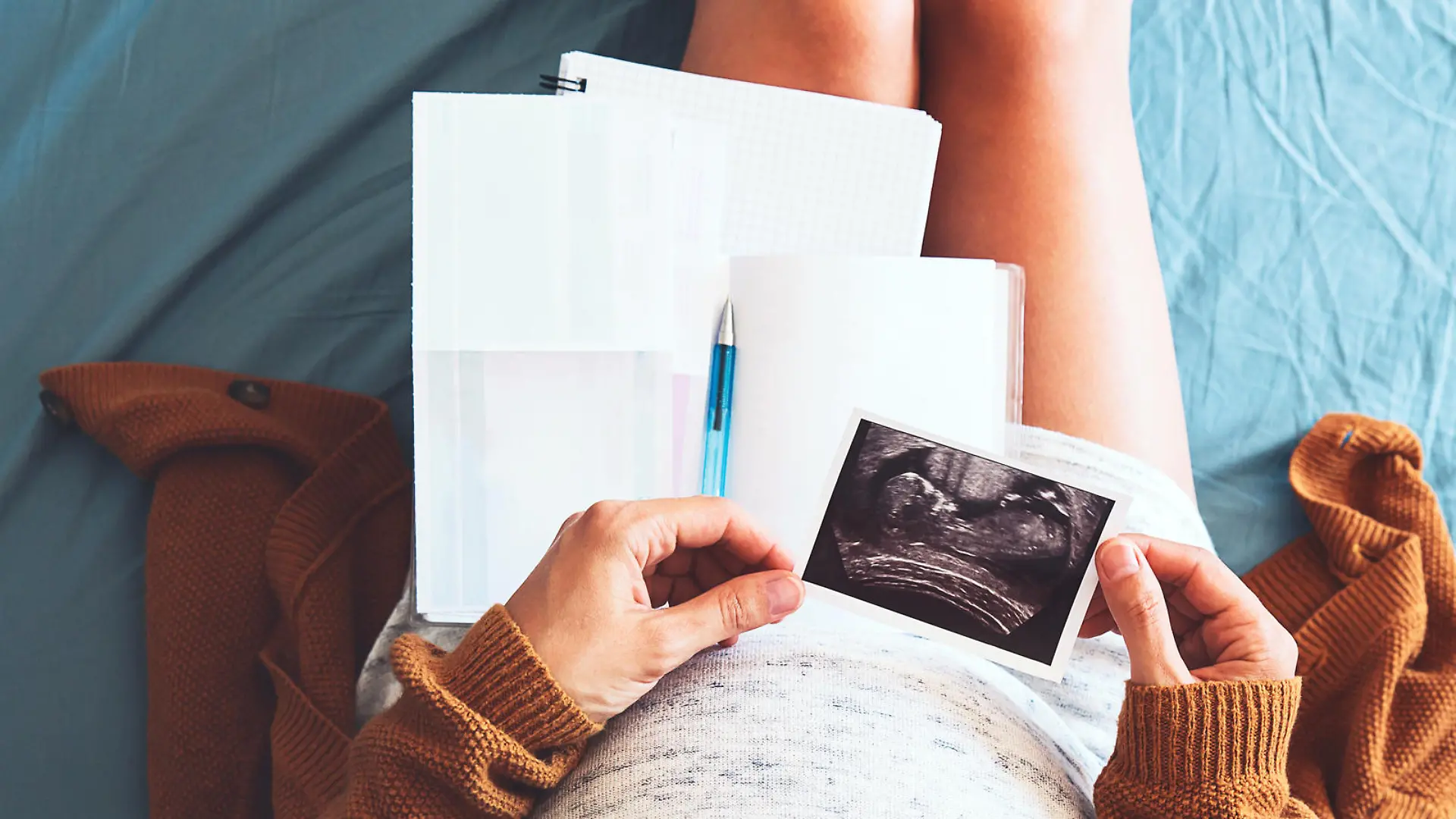 Pregnant woman makes notes, looking at ultrasound image and medical documents. Concept of pregnancy, health care, gynecology, medicine. Mother waiting of baby. Close-up, copy space, indoors.