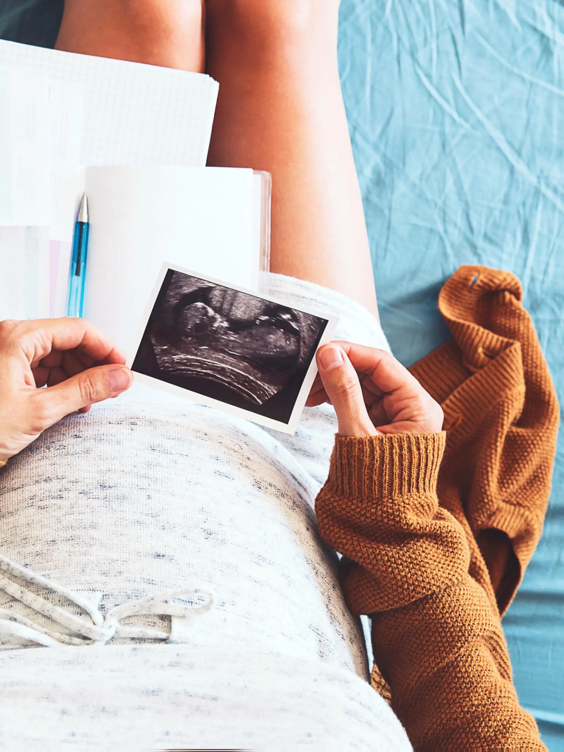 Pregnant woman makes notes, looking at ultrasound image and medical documents. Concept of pregnancy, health care, gynecology, medicine. Mother waiting of baby. Close-up, copy space, indoors.