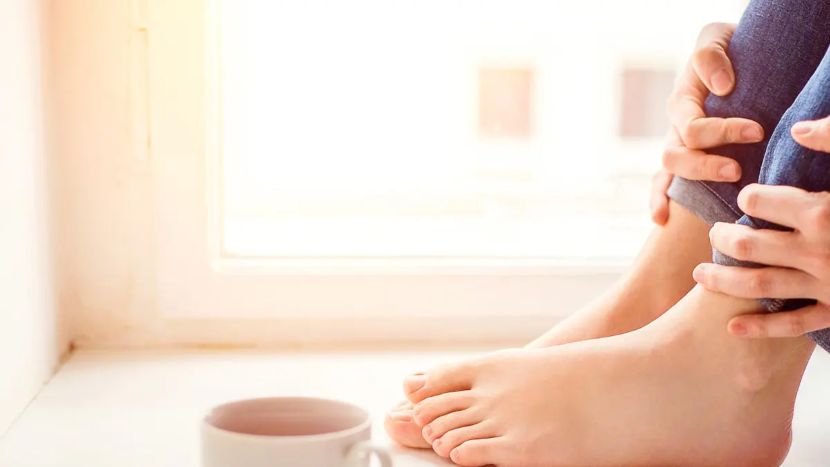 Feet of unrecognizable woman sitting on window sill with smart phone and cup of coffee