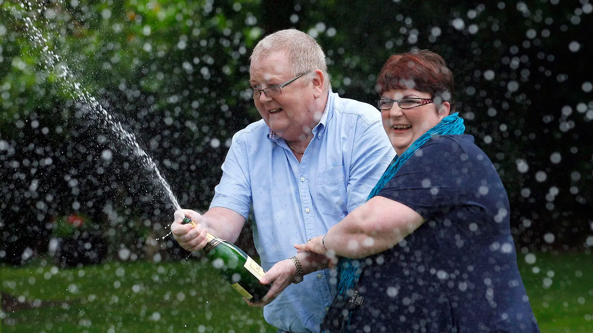 Colin Weir (R) and his wife Chris spray a bottle of champagne after a news conference at a hotel near Falkirk, Scotland July 15, 2011. The couple scooped 161 million pounds ($259 million) in Tuesday's Euromillions jackpot. REUTERS/David Moir (BRITAIN - Tags: SOCIETY)