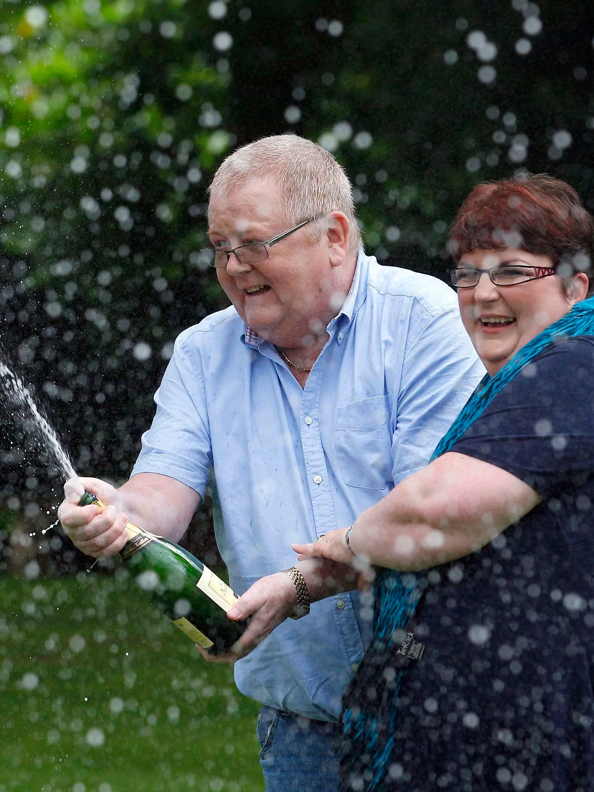 Colin Weir (R) and his wife Chris spray a bottle of champagne after a news conference at a hotel near Falkirk, Scotland July 15, 2011. The couple scooped 161 million pounds ($259 million) in Tuesday's Euromillions jackpot.   REUTERS/David Moir (BRITAIN - Tags: SOCIETY)