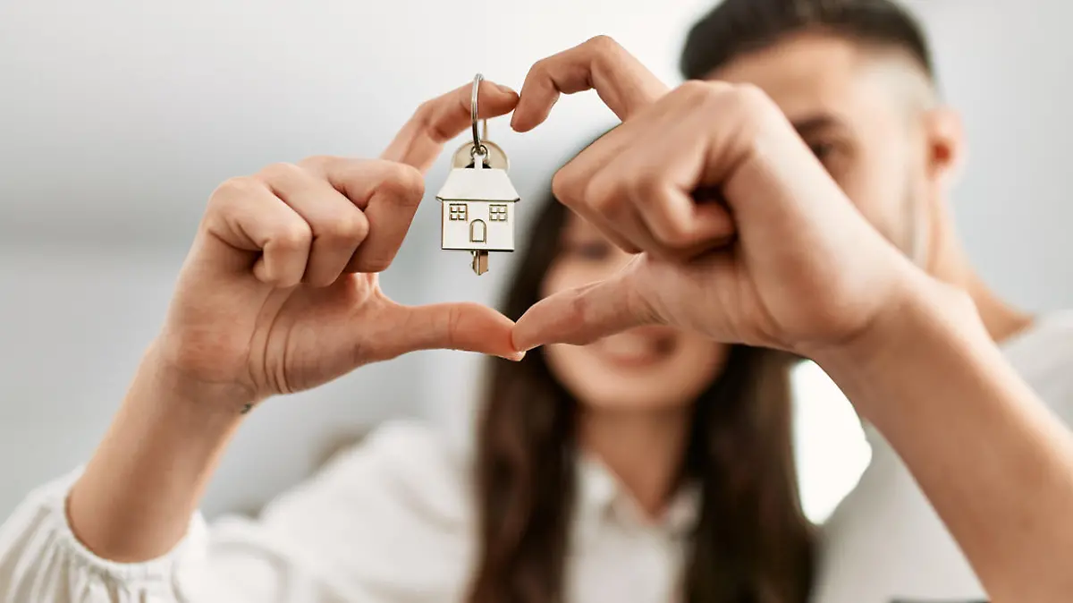 Young hispanic couple doing heart symbol with fingers and holding key of new home.