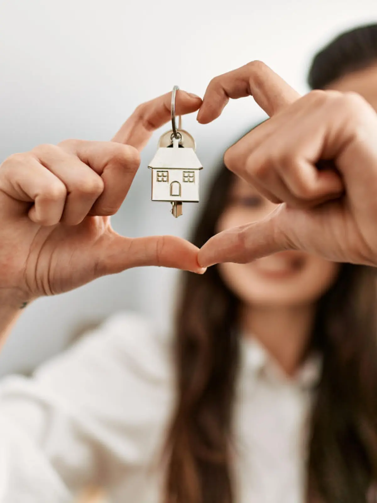 Young hispanic couple doing heart symbol with fingers and holding key of new home.