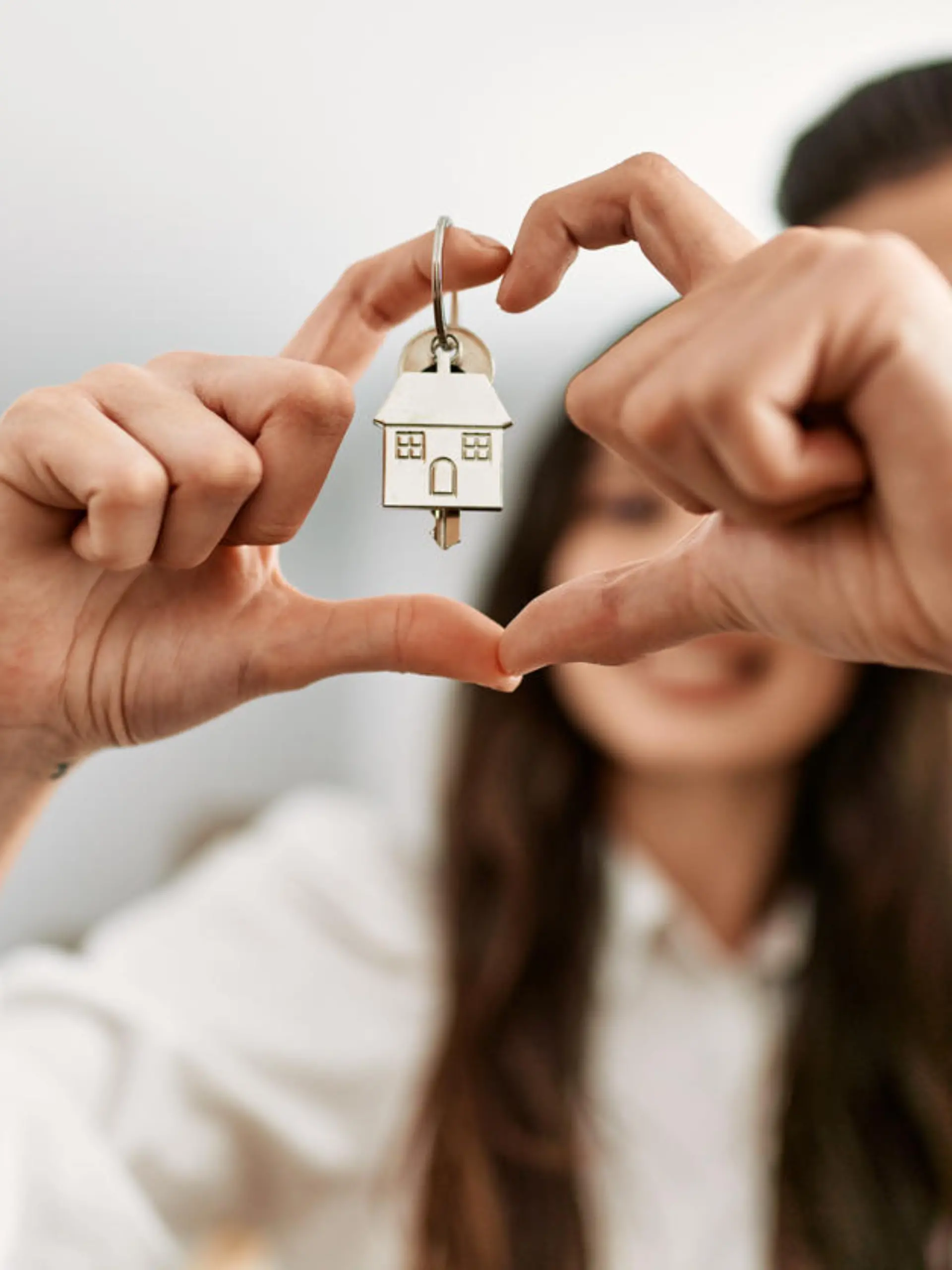Young hispanic couple doing heart symbol with fingers and holding key of new home.