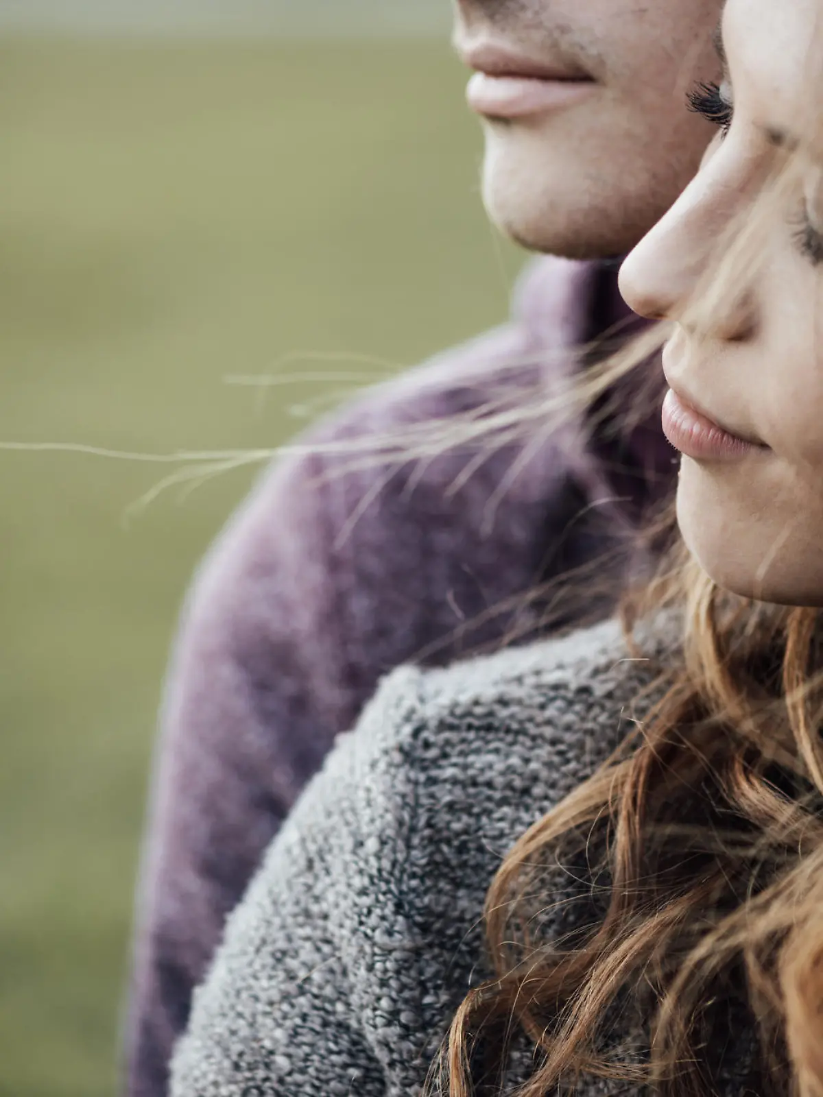 Young loving couple outdoors sitting on grass, hugging and looking away, future and relationships concept