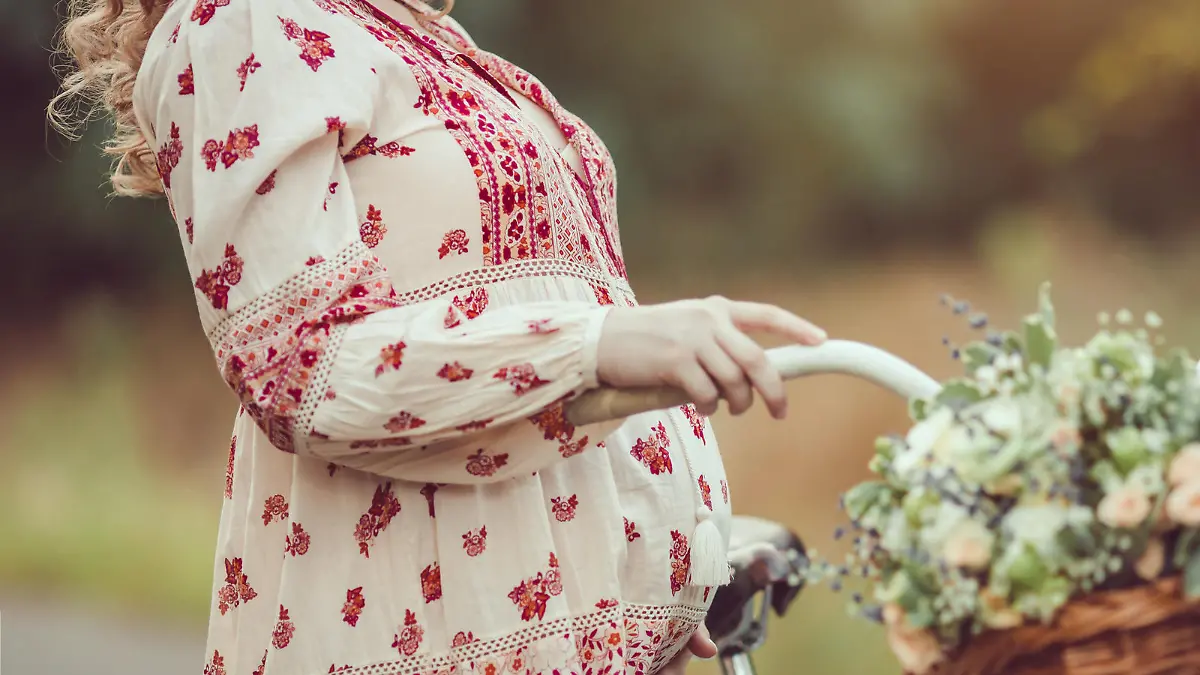 Pregnant belly against nature close-up. Pregnant girl retro French style with bicycle on a forest road. Beautiful pregnancy concept. Blonde happy woman with curly hair on nature background.