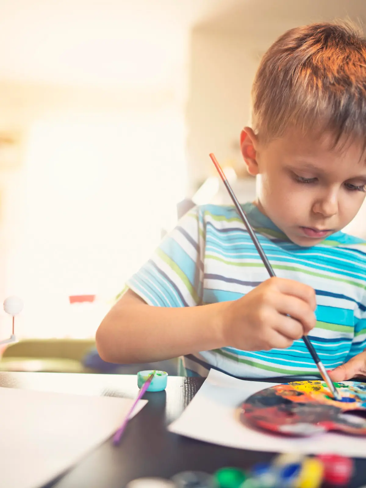 Little boy preparing his science school project. The boy aged 5 is painting a model of solar system.