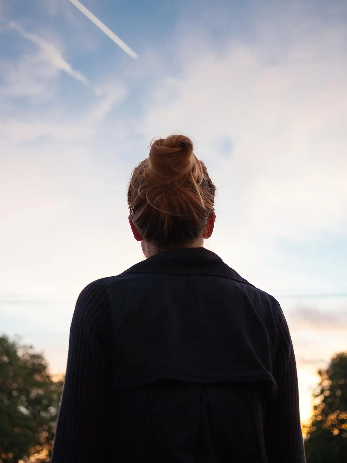 The silhouette of a young woman looking at sunset in the distance.