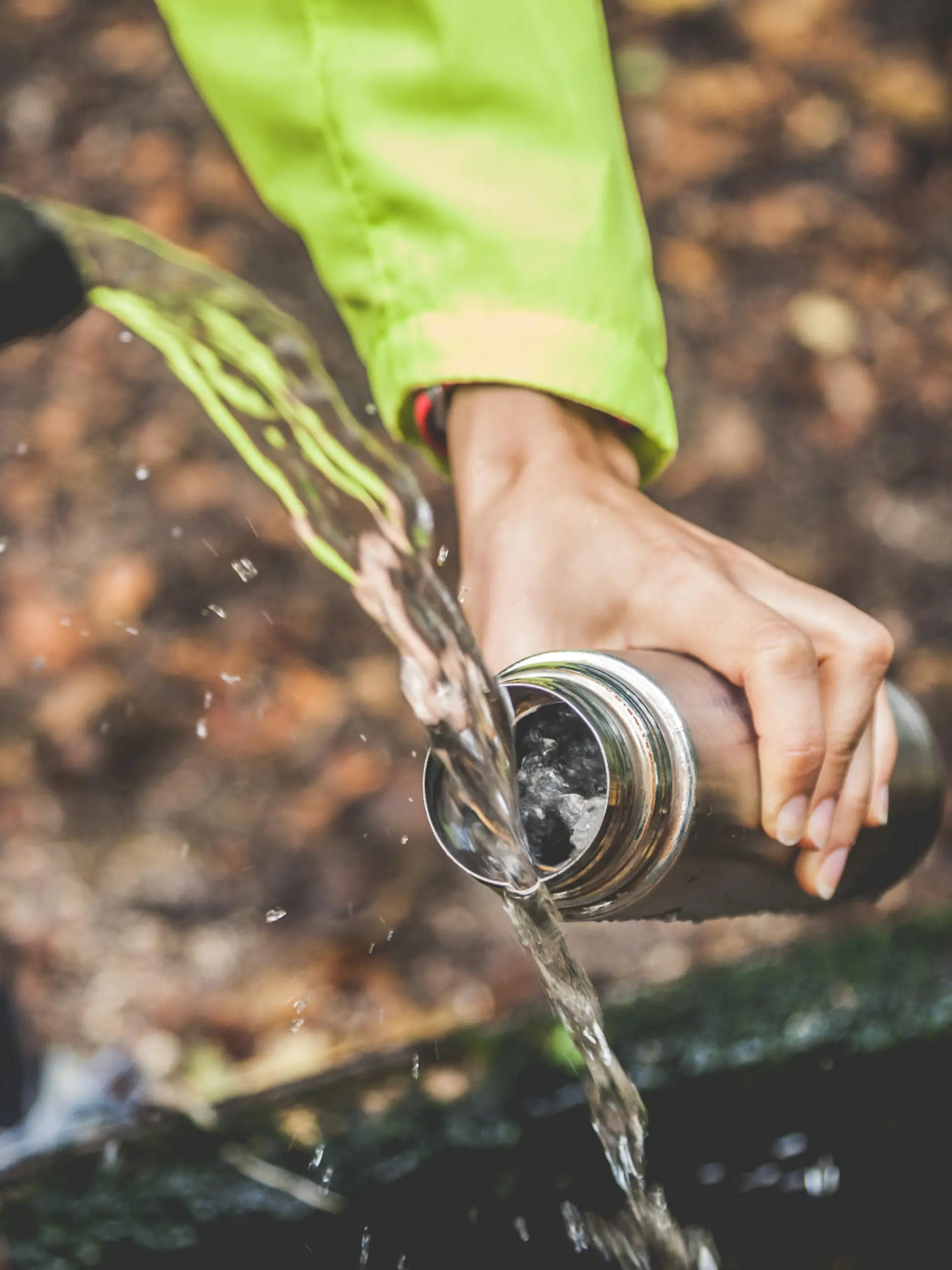 One woman refill water bottle from a source of water in mountain.