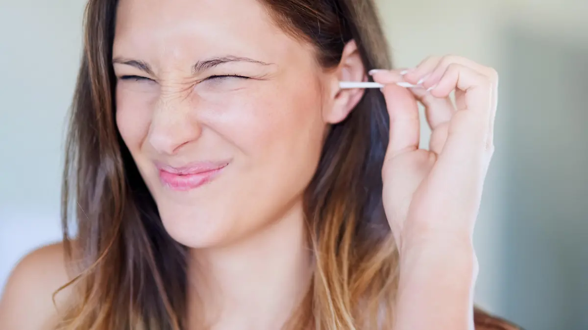 Shot of young woman pulling a funny face while cleaning her ear with an earbud at home