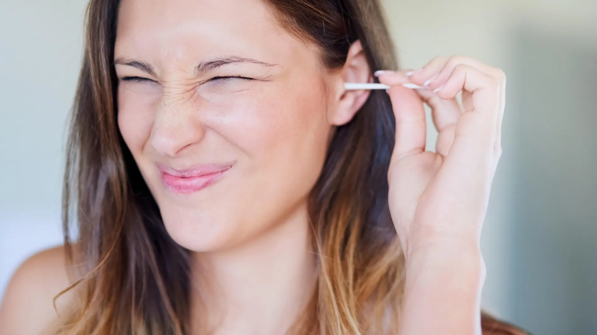 Shot of young woman pulling a funny face while cleaning her ear with an earbud at home