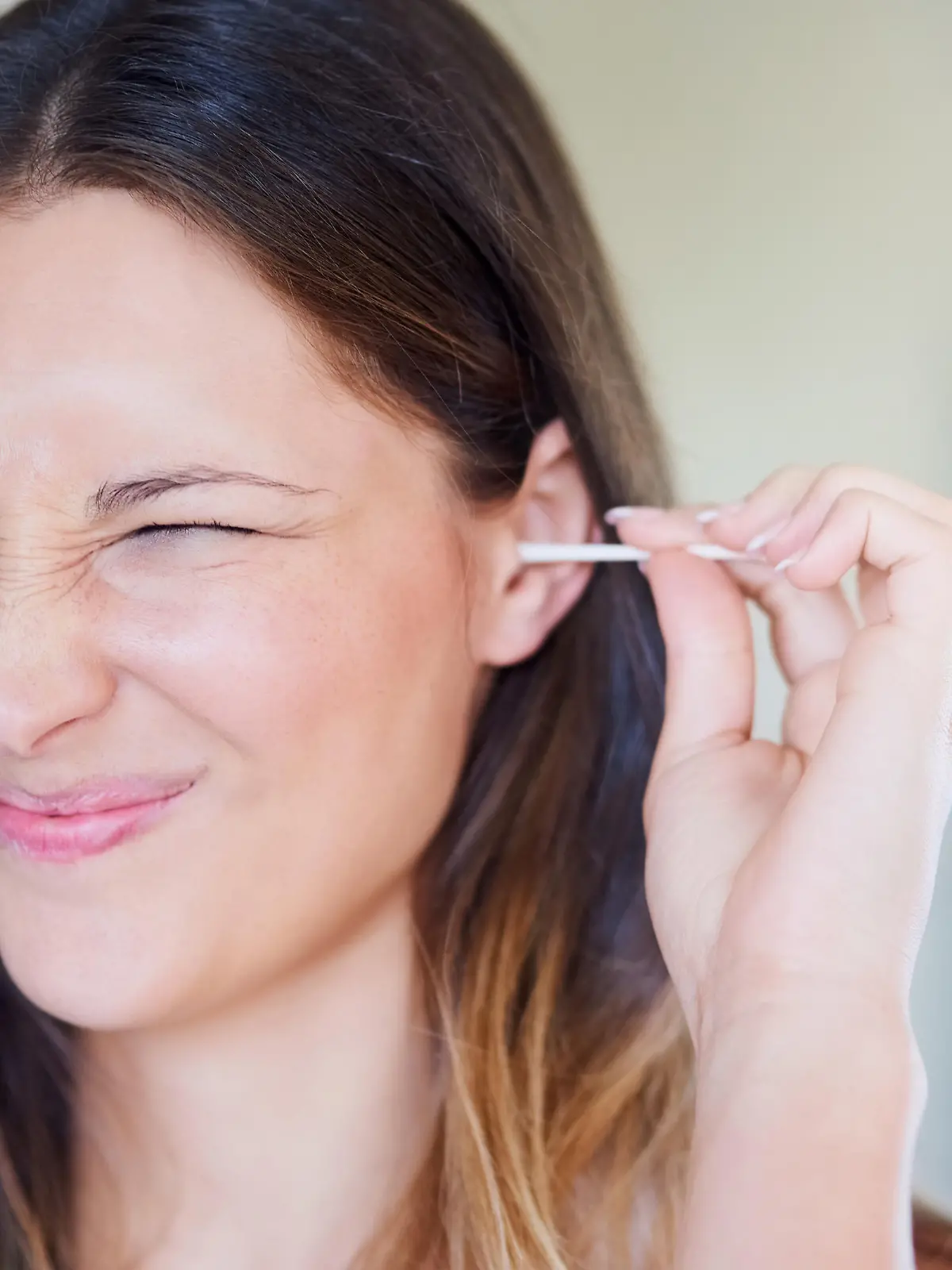 Shot of young woman pulling a funny face while cleaning her ear with an earbud at home