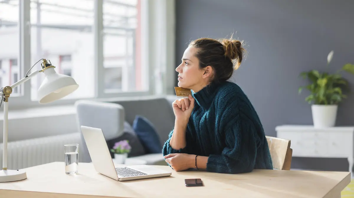  Profile of pensive woman with laptop and credit card sitting at desk at home looking out of window model released Symbolfoto property released PUBLICATIONxINxGERxSUIxAUTxHUNxONLY MOEF01854