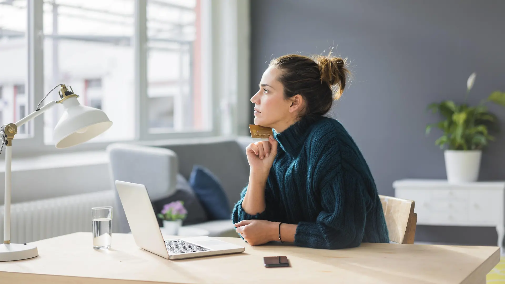 Profile of pensive woman with laptop and credit card sitting at desk at home looking out of window model released Symbolfoto property released PUBLICATIONxINxGERxSUIxAUTxHUNxONLY MOEF01854