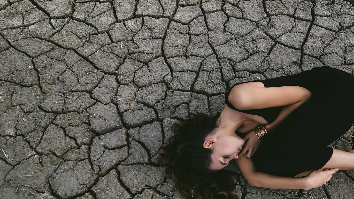 Beautiful young girl on the cracked earth in black dress