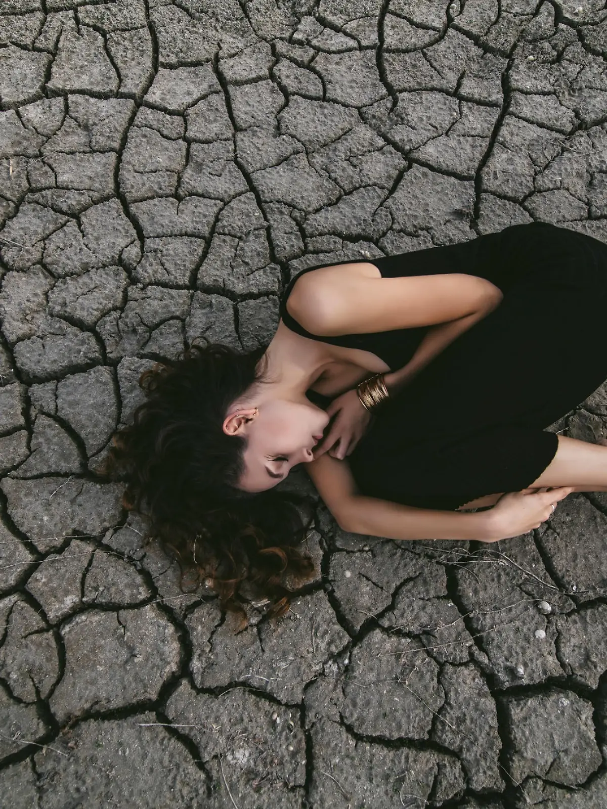 Beautiful young girl on the cracked earth in black dress