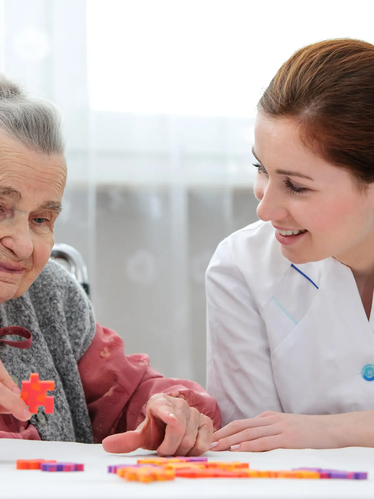 Elder care nurse playing jigsaw puzzle with senior woman in nursing home