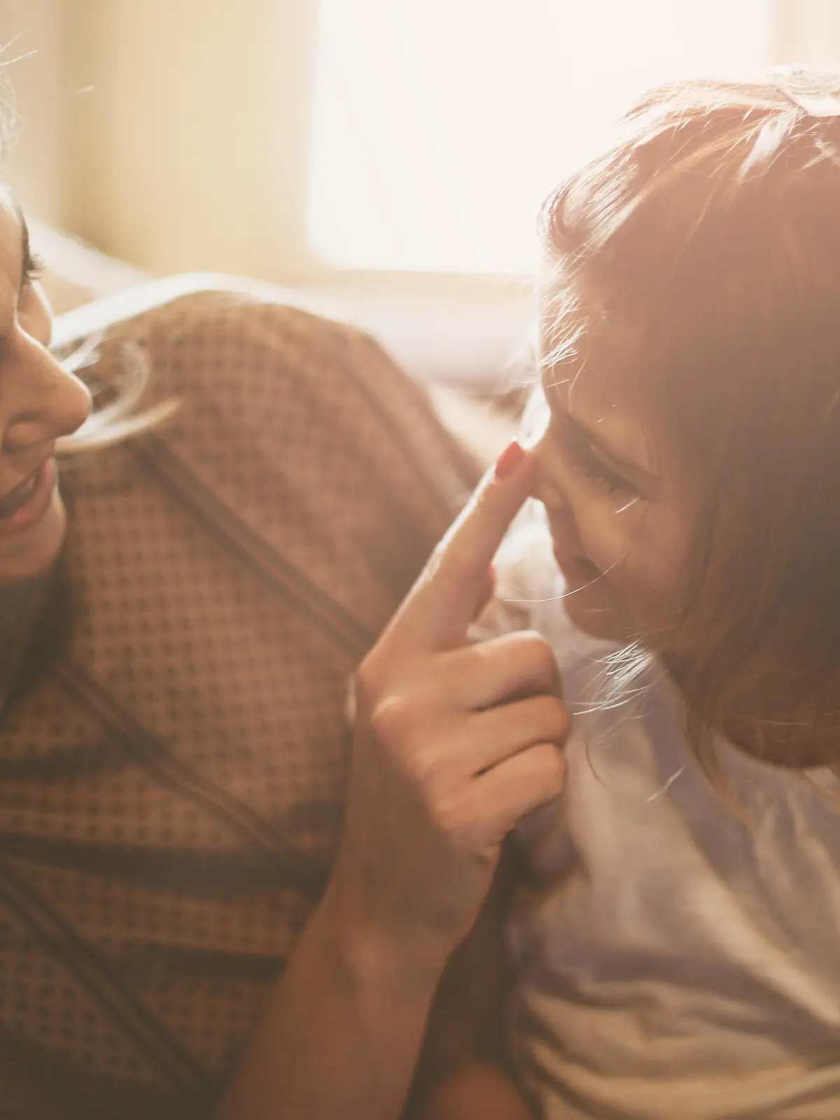 Mother and daughter are having fun at home. Mother touching daughter's nose.