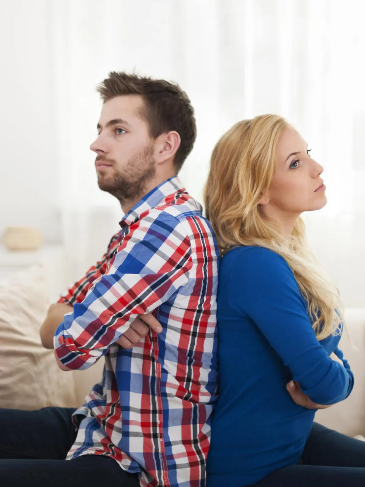 Angry young couple sitting back to back at home 