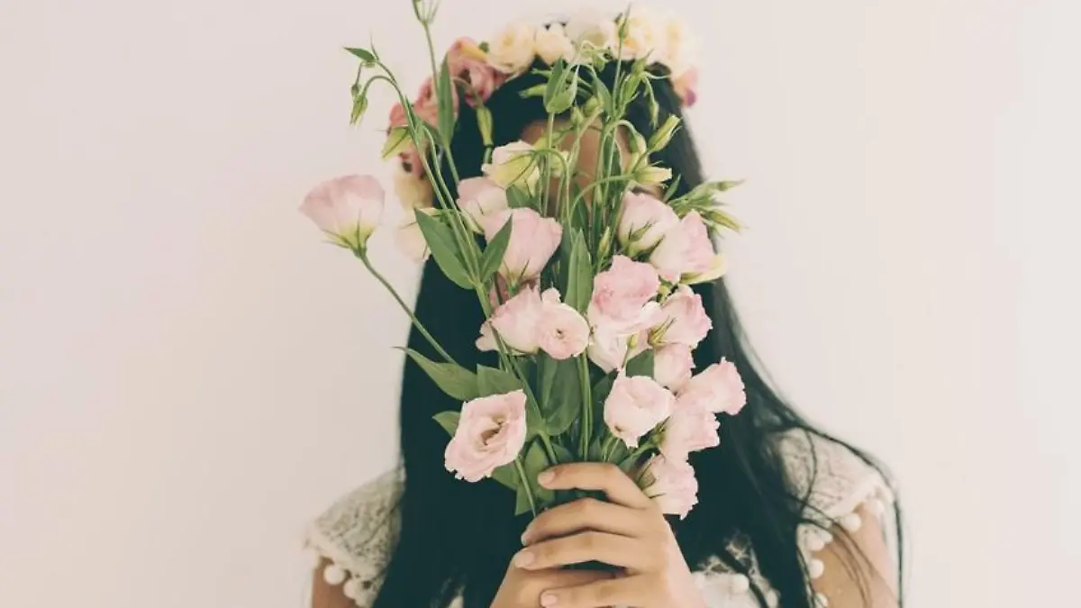 Woman holding pink flowers and hiding behind it