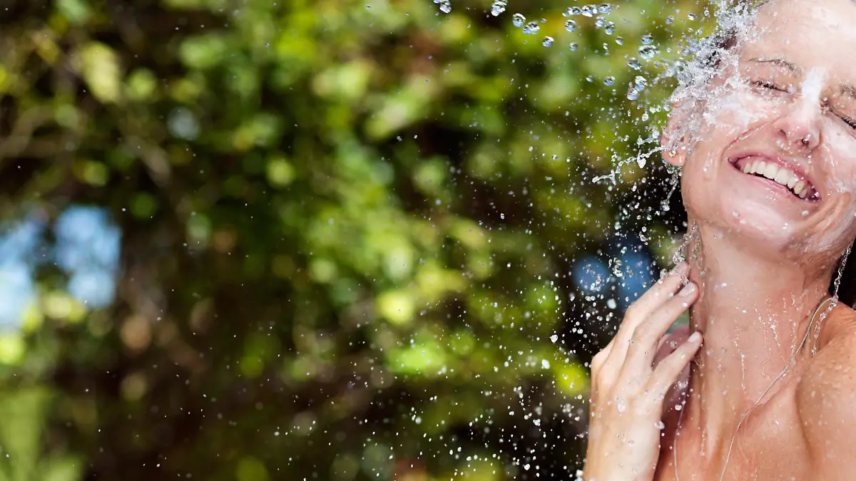 Frau mit Sonnencreme wird mit Wasser nass gemacht.