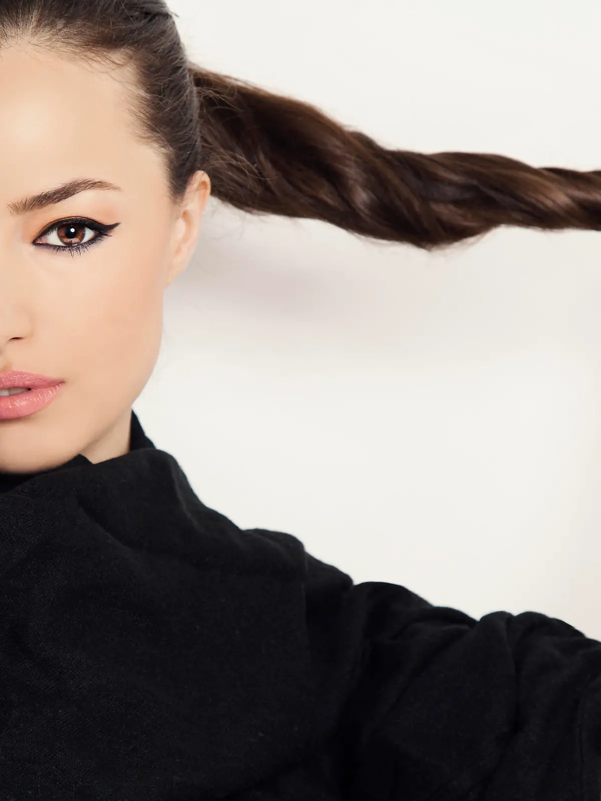 beautiful brunette holds her long ponytail, studio white