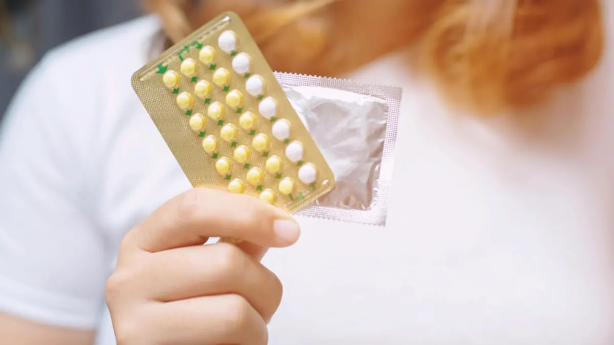 Woman hands give birth control pills and condom in hand. Taking Contraceptive Pill. safe sex concept on the bed Prevent infection and Contraceptives control the birth rate or safe prophylactic.