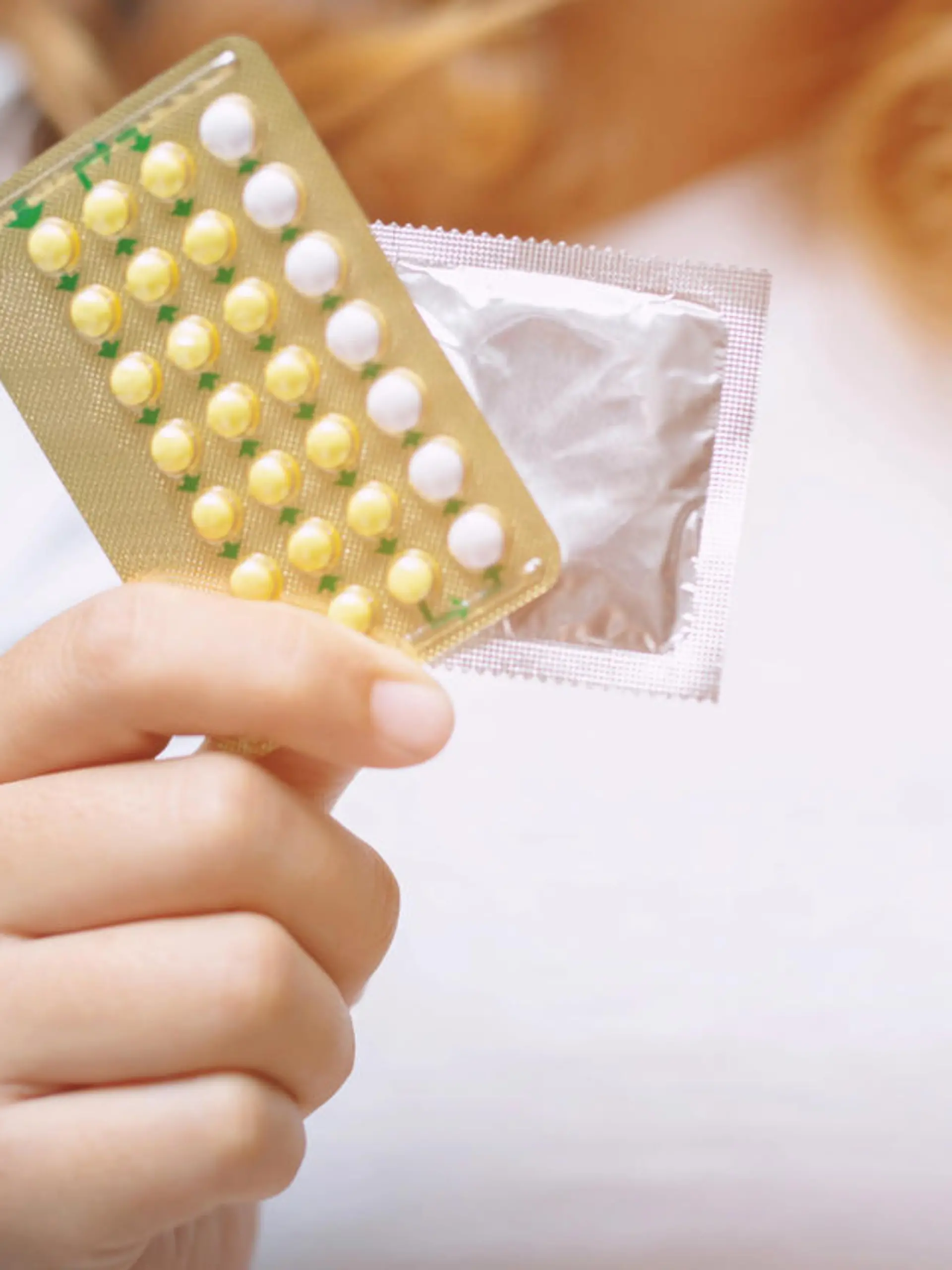 Woman hands give birth control pills and condom in hand. Taking Contraceptive Pill. safe sex concept on the bed Prevent infection and Contraceptives control the birth rate or safe prophylactic.