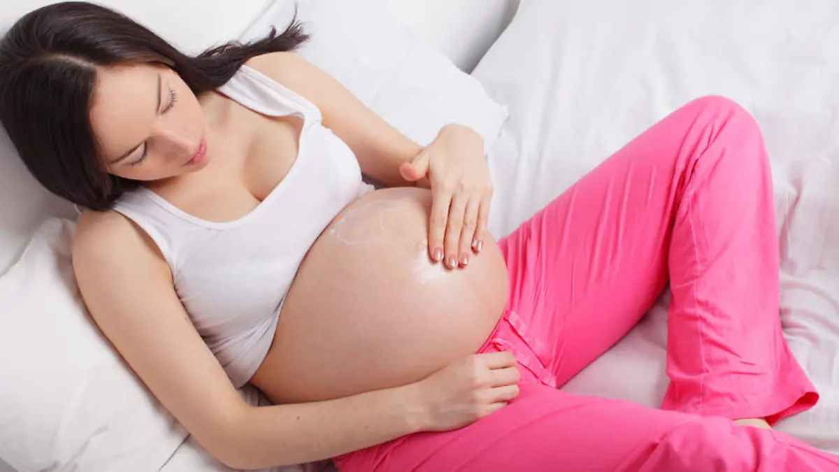 Pregnant woman putting a cream on a stomach at home