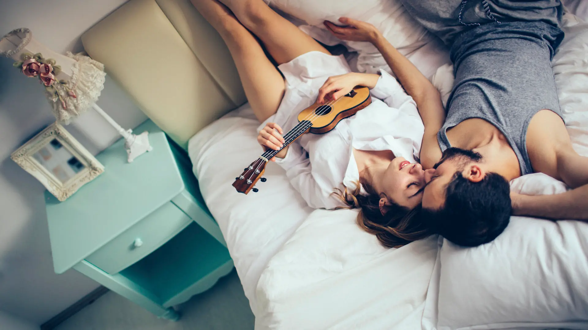 Lovely couple in pyjamas spending morning in their bed, celebrating Valentine's day by playing an ukulele 