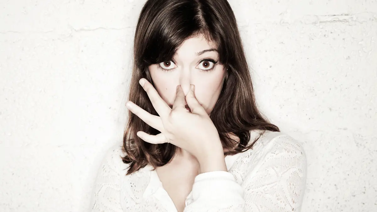 Portrait of a beautiful young woman staring into the camera with her eyes wide open and covering her nose with two fingers. Apparently something stinks.