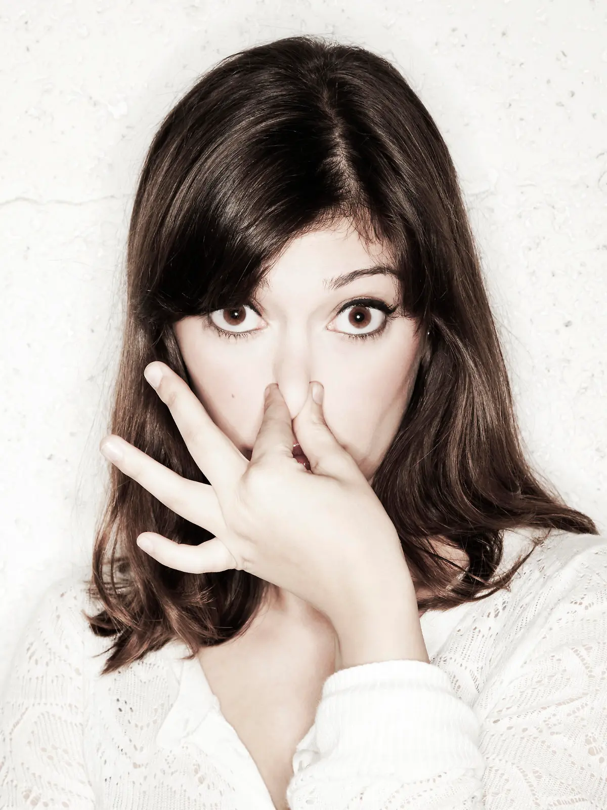 Portrait of a beautiful young woman staring into the camera with her eyes wide open and covering her nose with two fingers. Apparently something stinks.