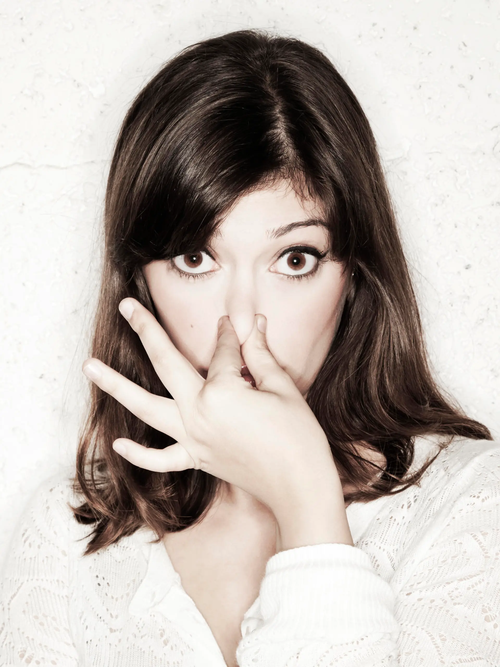 Portrait of a beautiful young woman staring into the camera with her eyes wide open and covering her nose with two fingers. Apparently something stinks.