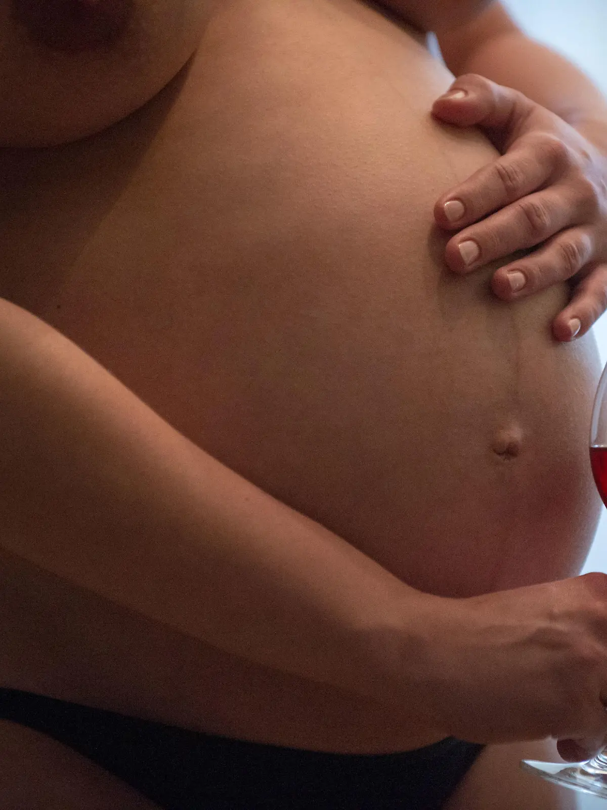 Eine nackte junge schwangere Frau hält ein Glas Wein in der rechten Hand, während die linke auf ihrem Bauch liegt. Foto: Hans Wiedl . Foto: Hans Wiedl  - Model Released