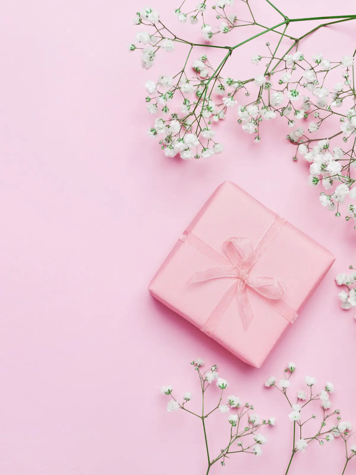 Gift or present box and flower on pink table from above. Pastel color. Greeting card. Flat lay style.