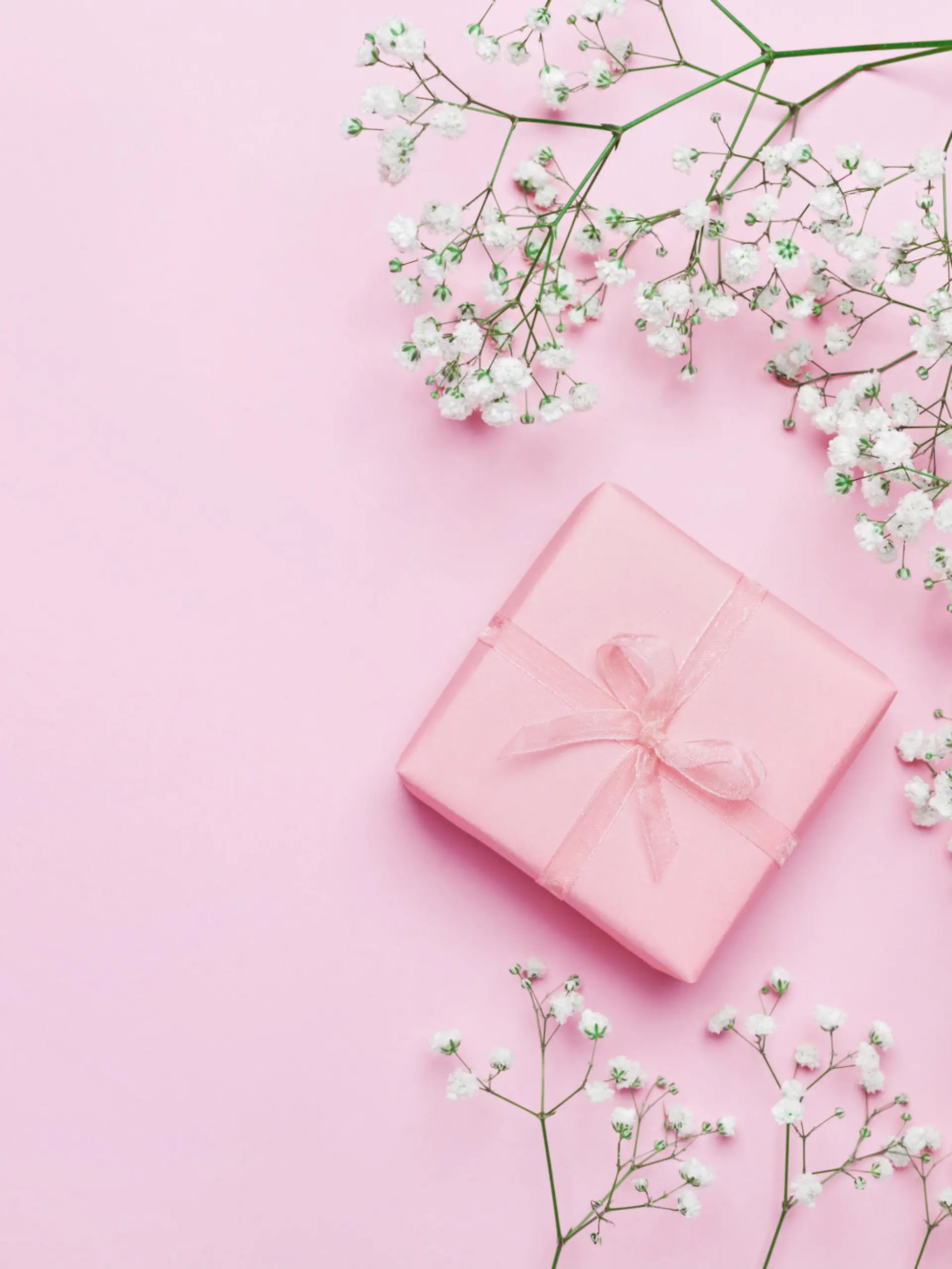 Gift or present box and flower on pink table from above. Pastel color. Greeting card. Flat lay style.