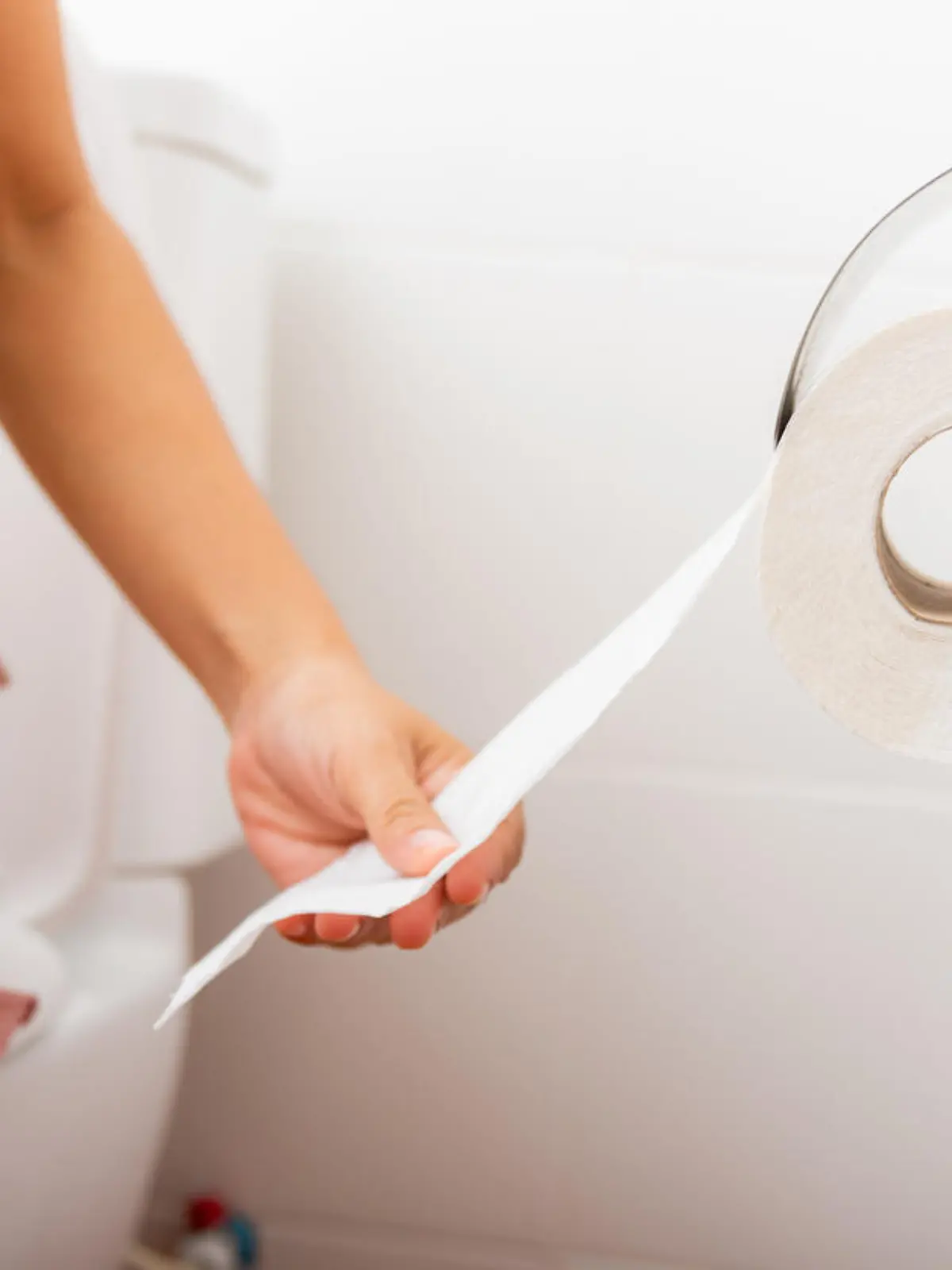 Closeup hand pulling toilet paper roll in holder for wipe, woman sitting on toilet she taking and tearing white tissue on wall to towel clean in bathroom, Healthcare concept