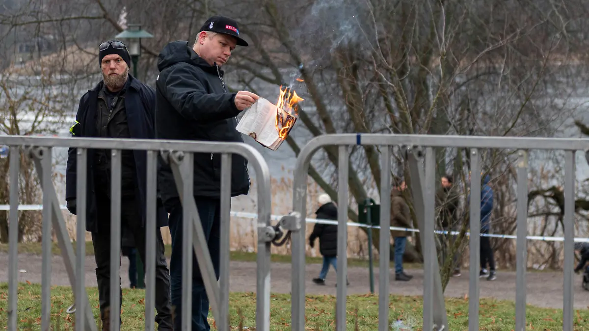 21.01.2023, Schweden, Stockholm: Der rechtsextreme Politiker Rasmus Paludan verbrennt in der Nähe der türkischen Botschaft einen Koran. Paludan erhielt von der Stockholmer Polizei die Erlaubnis, eine Demonstration für die Meinungsfreiheit abzuhalten und seinen Unmut über den türkischen Präsidenten Erdogan zu bekunden. Während der Aktion zeigte Paludan auch eine Karikatur des Propheten Mohammed. Links steht ein Polizist. Foto: Joel Lindhe/ZUMA Press Wire/dpa +++ dpa-Bildfunk +++
