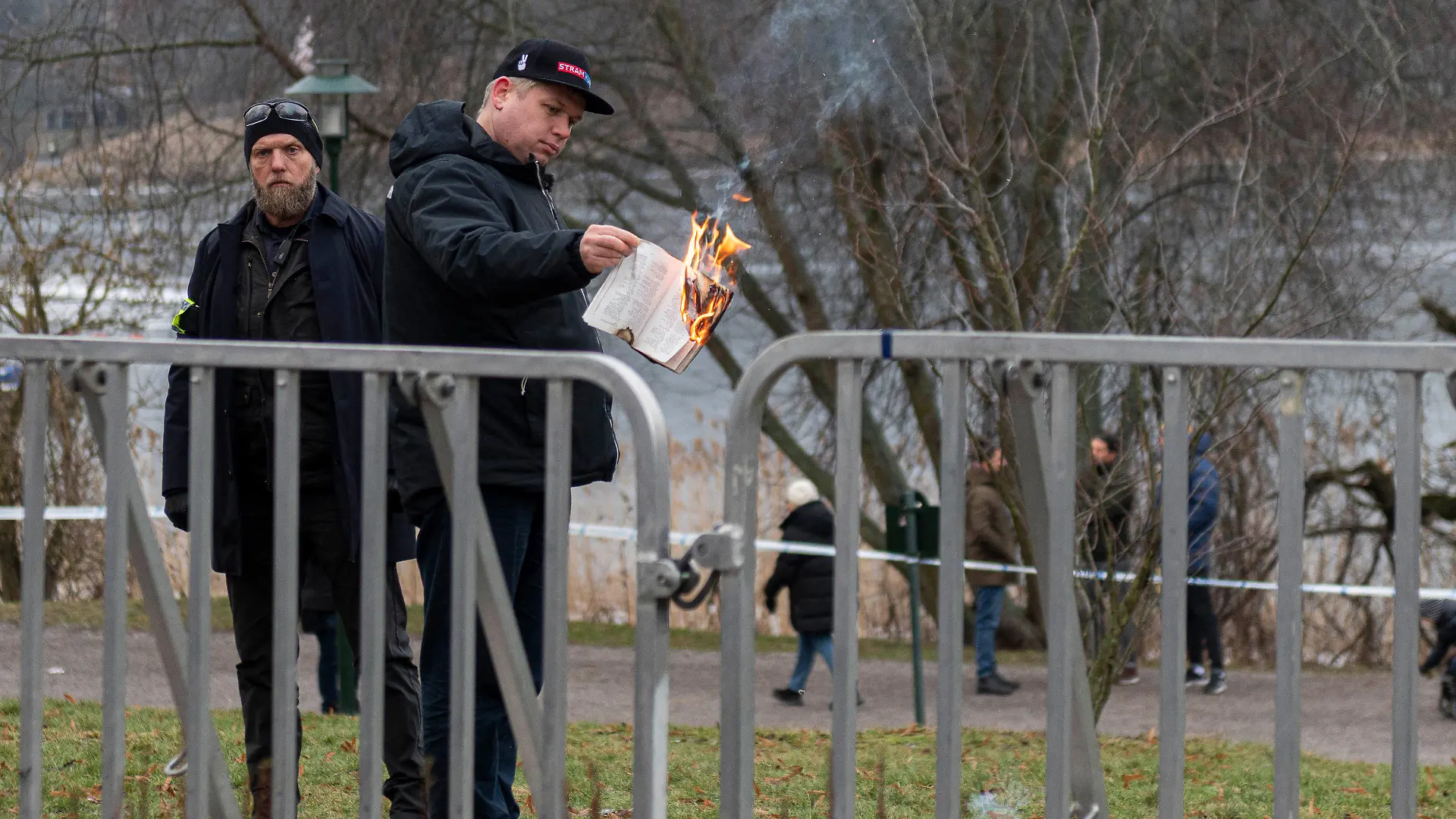 21.01.2023, Schweden, Stockholm: Der rechtsextreme Politiker Rasmus Paludan verbrennt in der Nähe der türkischen Botschaft einen Koran. Paludan erhielt von der Stockholmer Polizei die Erlaubnis, eine Demonstration für die Meinungsfreiheit abzuhalten und seinen Unmut über den türkischen Präsidenten Erdogan zu bekunden. Während der Aktion zeigte Paludan auch eine Karikatur des Propheten Mohammed. Links steht ein Polizist. Foto: Joel Lindhe/ZUMA Press Wire/dpa +++ dpa-Bildfunk +++