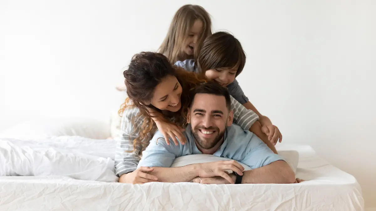 Portrait of happy young parents and small preschooler kids lying on white mattress in bedroom look at camera together, smiling family with little children relax on bed have fun, furniture concept